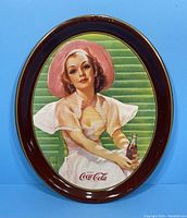 Full view of vintage oval tin tray with Coca Cola illustration and burgundy border against blue background
