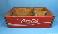 Front and side view of the red wooden Coca Cola crate showing logo and minor wear.