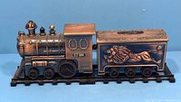 Front and side view of copper vintage train lighter and cigarette case. Shows engine details and lion embossed cigarette case.