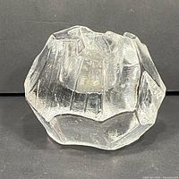 Clear glass faceted votive candle holder with uneven rock-like textured pattern.