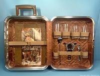 Open metal carry case showing the items inside including four glasses, bar tools, and a vintage booklet.
