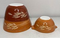 Three vintage Pyrex ceramic mixing bowls stacked and displayed showing Autumn Harvest Wheat pattern in brown, orange, and mustard yellow colors, viewed upside down to show exterior design.