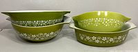 Four green Pyrex mixing bowls nested in pairs showing white daisy floral pattern and pouring spouts/handles