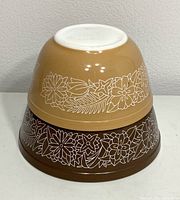 Photo of the bottom view of two stacked Pyrex Woodland bowls in brown and mustard yellow with white floral exterior pattern.