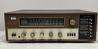 Front view of receiver showing tuning dial, logo badge, control knobs and wood veneer case