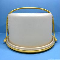 Side view of vintage Tupperware cake carrier showing cream lid and yellow handle and base. Minor wear visible.