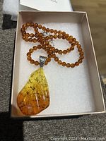 Necklace with amber beads and a large amber pendant in a white box with foam insert, close-up showing pendant and bead detail