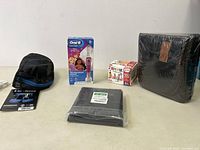 Full view of all items in the lot on a light-colored surface including black harness bag, oral-b toothbrush box, toy box, black seat cover.