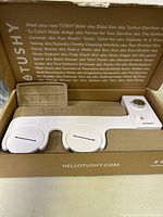 View of the bidet unit in the open box with protective inserts and branding text visible.