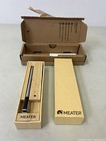 Meater wireless smart meat thermometer probe resting in wooden storage/charging box with open lid and outer cardboard packaging visible