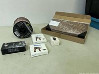 Full view of the lot showing a spool of speaker wire, two boxes of Wingo guitar capos, Aromk tuner box, and coin holder box on a table