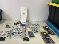Assorted metal hardware parts, wire spool, clamps and screws laid out on a flat surface.