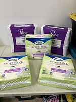 Five packs of women's pads: three Tena Sensitive Care and two Poise Fresh Protection