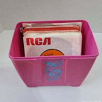 Pink storage container filled with 45 RPM vinyl records in paper sleeves showing multiple labels including RCA