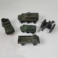 Four army vehicle toys: three green military vehicles and one black artillery cannon on white background.