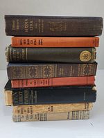 Spine view of 8 vintage hardcover books showing varying degrees of wear and different colored bindings.
