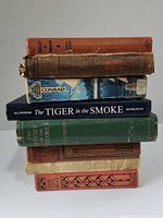 Stack of seven hardcover books displayed with varying spine damage and tape repairs.