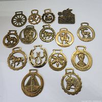 Photo of all 14 brass bottle openers arranged on a white background showing various designs including animals, portraits, and thematic motifs.