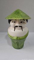 Front view of ceramic cookie jar shaped as a man with a green textured conical hat and green robe