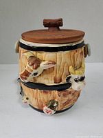 Front view of the ceramic cookie jar showing textured wood grain barrel design with cow head handles and detailed lid handle.