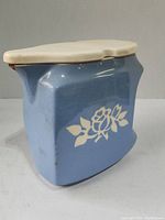 Side view of blue ceramic cookie jar showing white floral motif and cream lid