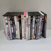 Photo of 18 DVDs lined up showing spine titles including Saving Private Ryan, The Big Bang Theory seasons, 27 Dresses, Cinderella Man, and others