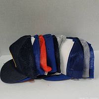 Side view of stacked trucker hats showing various colors including black, blue, red, white, and gray mesh backs.
