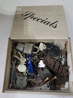 Box of various locks, keys, and metal hardware parts including padlocks, keys on rings, and metal brackets.