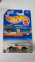 Packaged Hot Wheels toy car, white Mustang Cobra with orange graphics in blue card packaging labeled Mega Graphics Series