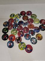 Several pogs laid out on white surface showing multiple colorful designs including Spider-Man, Roxx, and other patterns.