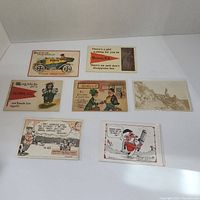 Seven vintage postcards placed on a white surface featuring humorous cartoon illustrations and text, some referencing Victoria, B.C.