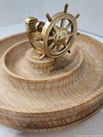 Close-up angled view of the brass ship wheel nutcracker mounted on a carved wooden tray.