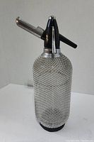 Front view of the vintage soda syphon spray bottle showing the wire mesh, black nozzle, and metal spout.