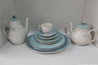 Tea set arranged with two teapots, one cup with stack of plates and saucers, showing floral design and general look of the set.