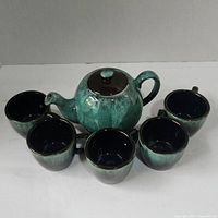 Photo of green ceramic teapot surrounded by five matching cups showing overall set configuration and colors.