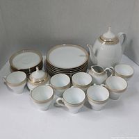 Full view of tea set items arranged showing teapot, cream pitcher, sugar bowl, cups, saucers, and plates with gold decorative trim on white porcelain.