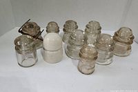 Top angled view of 11 vintage electrical insulators including clear glass and white ceramic pieces arranged on a white surface.