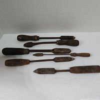 Six vintage soldering irons laid out on white background showing wood handles and metal tips.