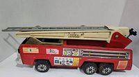 Side view of the vintage Tonka fire truck showing red body, cream ladder with Tonka branding and decals.