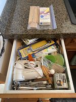 Open drawer showing miscellaneous small kitchen and baking tools including electric mixer, melon ballers, rolling pin, wooden skewers, and disposable piping bags.