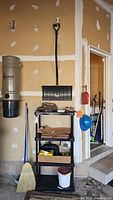 Photo showing broom, snow shovel, gloves, bucket, and brown lawn bags on a black shelf in a garage with beige walls.