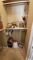Wide view of closet shelf and floor area showing vases, decorative candle holder, glass jar with metal lid, hangers, foot bath basin, and boxes
