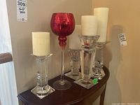 Clear and red glass candle holders with pillar candles arranged on wooden table, varying heights 8-16 inches.