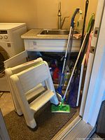 Step ladder folded leaning against wall with mop and duster nearby in laundry area