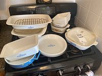 Wide view of entire lot on stove showing all dishes and bakeware including roaster, round platter, small dishes, and casserole with lid