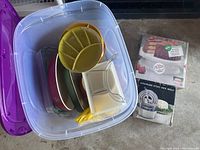 Tote bin filled with various dishes including divided trays, plates, and baking molds, some packaged items beside the bin