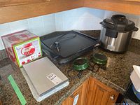 Overview of all kitchen appliances: electric griddle, Instant Pot, two green pot warmers, boxed popcorn maker, and a metal tray.