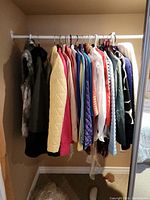 Photo of assorted jackets and vests in multiple colors hanging on white metal rod in closet, including quilted jackets and vests.