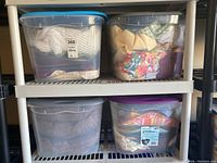 Four stacked large plastic bins containing assorted linens in various colors and patterns.