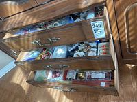 Three wooden drawers open displaying assorted napkin rings, coasters, candles, and other items inside.